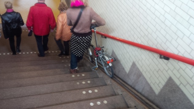 Steps in and out of a rail station with provision for wheeling a bike at the side. It's little things like these that add to the bicycling culture. Nice to see the bike being wheeled here is a Brompton! :) 